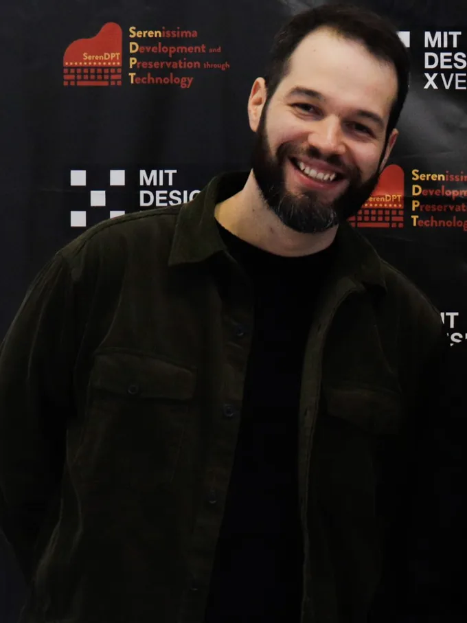 Riccardo Sponchiado sorride, in giacca scura, davanti al pannello di MIT DesignX Venice.
